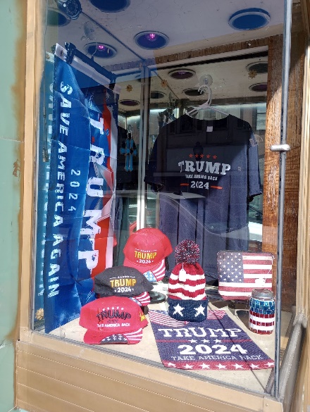 Storefront window filled with Trump 2024 hats, shirts, flags, and rugs